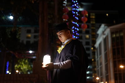 Young man wearing graduation gown at night