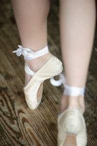 Low section of woman wearing ballet shoes dancing on hardwood floor