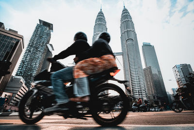 Low angle view of people riding motorcycle on street against petronas towers