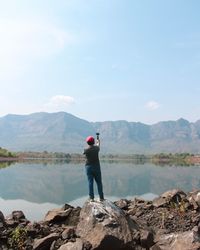 Man standing on rock looking at mountains against sky