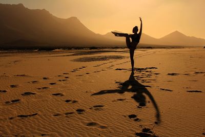 Silhouette person on sand at beach against sky during sunset