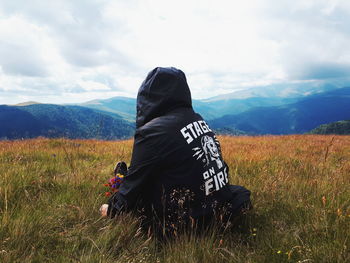 Rear view of woman sitting on field against mountain range