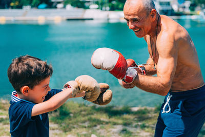 Shirtless grandfather with grandson boxing by swimming pool