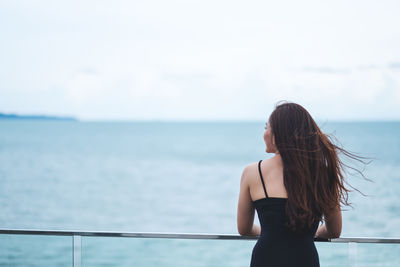 Rear view of woman standing by sea against sky