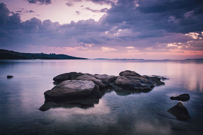 Rocks in lake against sky during sunrise