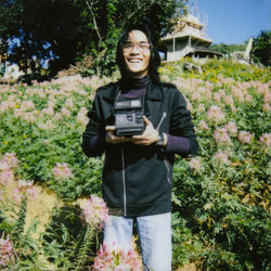 Portrait of smiling woman photographing while standing on plants