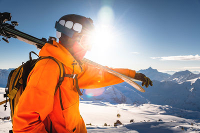 Male skier standing against snowy mountain during sunny day. ski resort concept