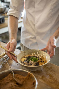 Midsection of man holding soup bowl on table in kitchen