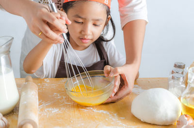 Midsection of mother and daughter whisking egg ag home