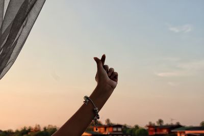 Close-up of hand against sky during sunset