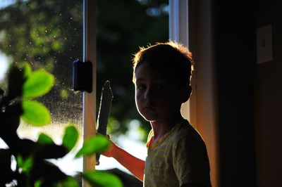 Portrait of boy holding toy while standing by window at home