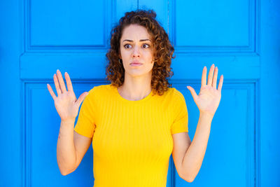 Portrait of smiling young woman gesturing against blue wall