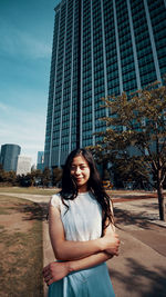 Portrait of smiling young woman standing against buildings in city