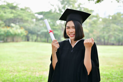 Student wearing graduation gown while standing on field at park