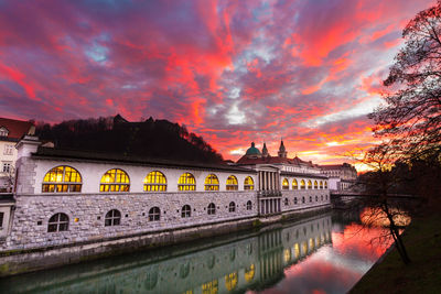 Bridge over river by buildings against sky during sunset