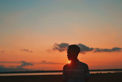 Rear view of woman looking at sea against sky during sunset