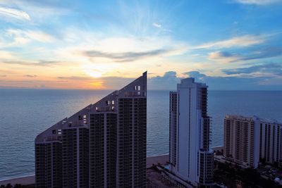 Modern building by sea against sky during sunset