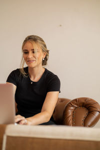 Young woman using laptop while sitting on sofa against wall