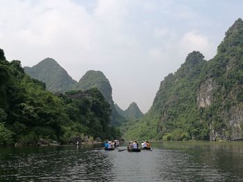 People in boats on river amidst mountains against sky