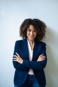 Smiling businesswoman with arms crossed in front of white wall