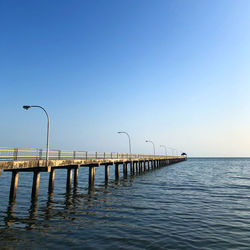 Pier over sea against clear blue sky