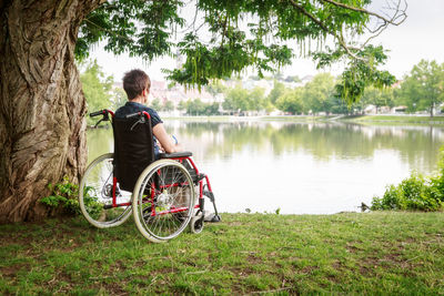 Man sitting on grass by lake against trees