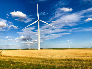 Wind turbines on field against sky