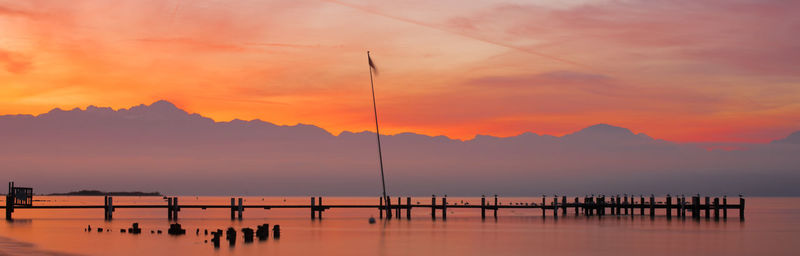 Silhouette wooden posts in sea against orange sky