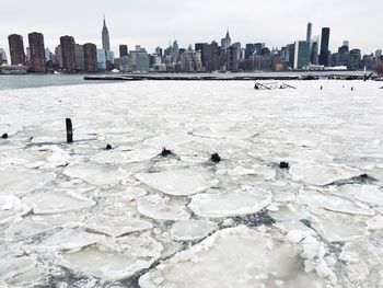 Frozen east river by city against sky