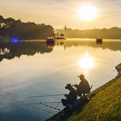Side view of silhouette men fishing in river during sunset