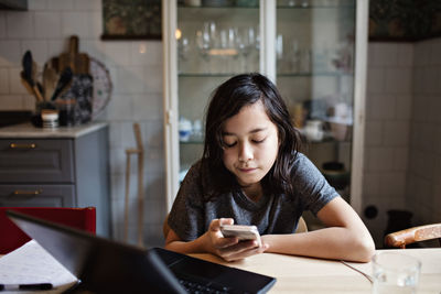 Young woman using phone while sitting on table