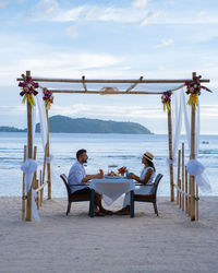 People sitting on table at beach against sky