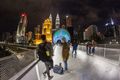 People walking on illuminated modern buildings in city at night