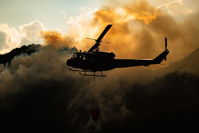 Low angle view of silhouette helicopter against smoke during sunset