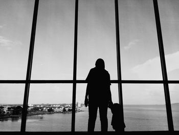 Silhouette mother with daughter standing by window against sea