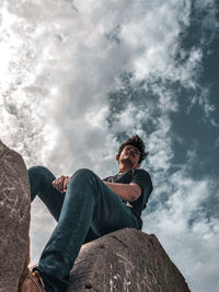 Low angle view of man sitting on rock against sky