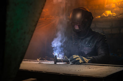 Village workshop, welding in an old garage. an unrecognizable man repairs a metal part wearing