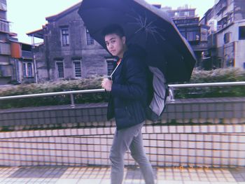 Side view of young man standing against railing in city