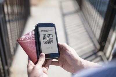 Hands holding smartphone with covid-19 vaccine certificate and passport