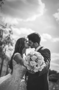 Close-up of couple holding flower against sky