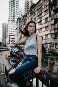 Young woman sitting on railing against building