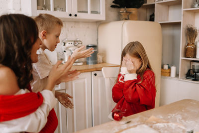 Mom and brother scold a roaring teenage girl in a red sweater in the kitchen at home on holiday