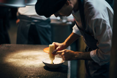 Crop professional chef pouring sauce on dish in elegant plate working on restaurant kitchen