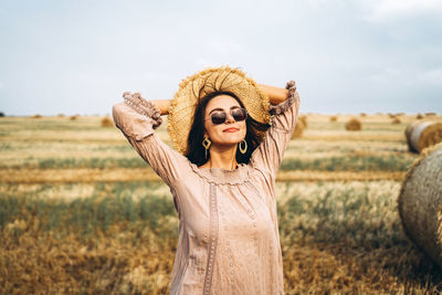 Smiling woman in sunglasses with bare shoulders on a background of wheat field and bales of hay.