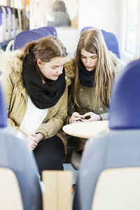 Young female friends using mobile phone while traveling in train