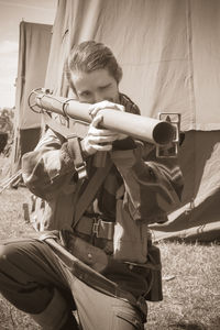 Man aiming through bazooka while crouching on field by tent