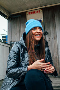 Smiling young woman wearing warm clothing while sitting outdoors