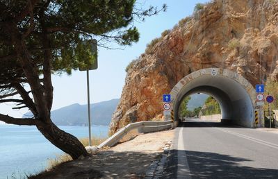 Road leading towards tunnel by sea on sunny day
