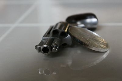 Close-up of revolver and coin on tiled floor