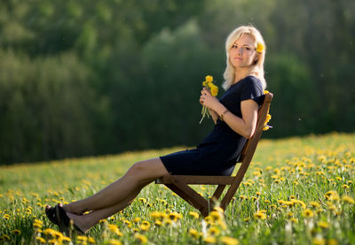 Portrait of young woman sitting on chair at dandelion meadow